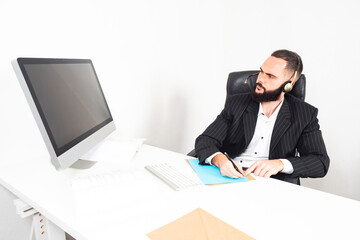 Poster - A man in headphones and a business suit. The man looks at the information on the computer and makes notes. A man at his Desk.