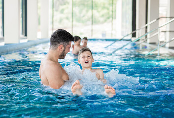 Wall Mural - smiling family of four having fun and relaxing in indoor swimming pool at hotel resort.