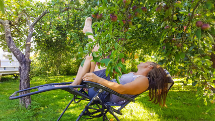 Middle-aged man with long hairs relaxing on a deck chair in the garden under a tree in summer time. Vacation and recreation concept.