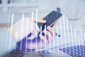 Double exposure of man's hands holding and using a digital device and forex graph drawing. Financial market concept.