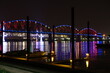 Lighted Rainbow Colored Bridge Over River With Boats At Night