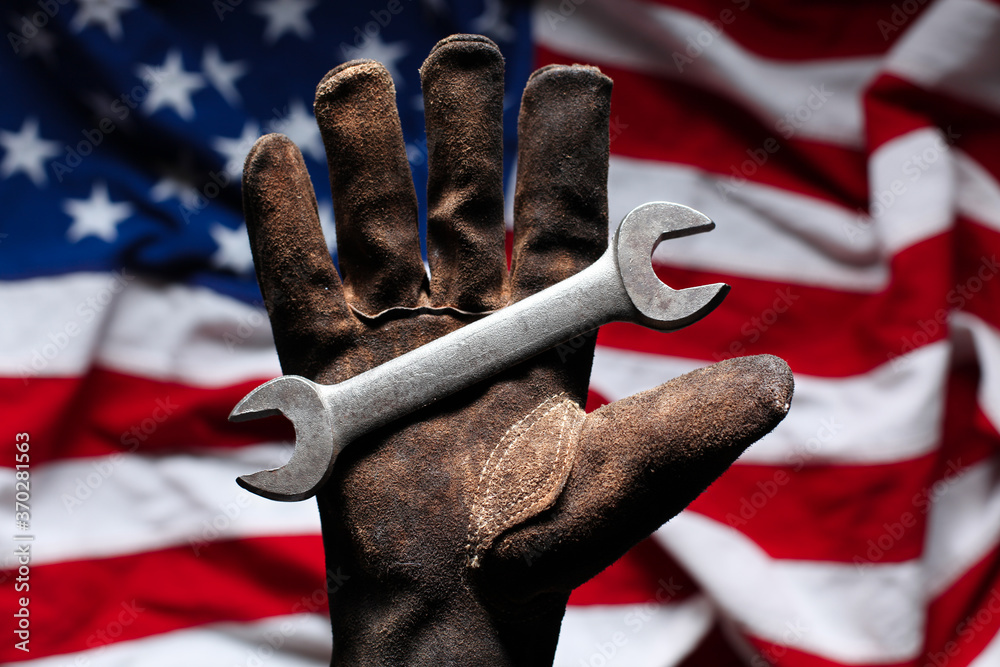 Hand in worn and dirty golve holding crescent wrench over American Flag - obrazy, fototapety, plakaty 