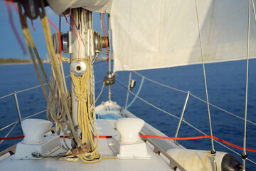 White yacht sailing in the Baltic sea after the rain at sunset. Riga, Latvia. Close-up view from the deck to the bow, mast and sails. Clear blue sky. Sport, recreation, leisure activity, travel