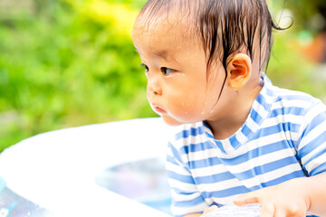 Wall Mural - 外で水遊びでずぶ濡れの子供　何かに気を取られて真剣なまなざしの子供のアップ