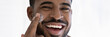 © fizkes - Close up head shot portrait overjoyed African American handsome young man applying moisturizing face cream, facial massage, enjoying skincare procedure, looking at camera, wide cropped image