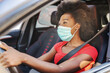 © dusanpetkovic1 - Young attractive african woman with mask on her face driving her car during covid-19 pandemic.