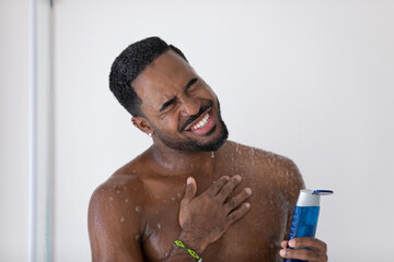 Wall Mural - Close up smiling overjoyed African American handsome young man taking shower, holding shampoo or moisturizing gel bottle, relaxing, standing in bathroom, enjoying morning routine procedure