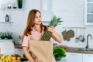 Wall Mural - Healthy food at home. Happy woman is showing pineapple in modern kitchen. Vegan and vegeterian lifestile.