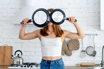 Wall Mural - Strong woman holding frying pans near eyes. Athletic woman with kitchen utensils. Healthy lifestyle