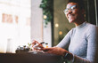 © BullRun - Cheerful afro american hipster girl in trendy outfit recreating in coffee shop making money transfer in online banking service using modern smartphone and free wifi access sitting in coffee shop