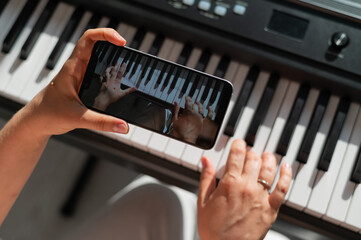 a girl watches an online music lesson on a smartphone and learns to play the piano. close-up of woma