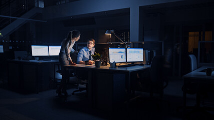 Aufkleber - Ambitious and Confident Businessman Uses Desktop Computer, His Female Project Manager Explains Specific Tasks, Account Handling and Strategic Moves. Professional People Late at Night in Big Office