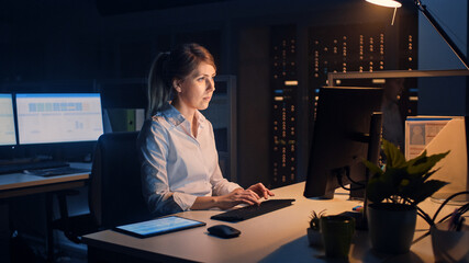 Poster - Portrait of Beautiful Businesswoman Uses Desktop Computer, Typing on a Keyboard, Monitoring Business Transactions, Signing Contracts. Works Late at Night in Big Corporate Office