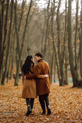 Young couple in love walking in the park on a autumn day. Enjoying time together. Stylish and loving couple enjoying each other in the autumn forest. 