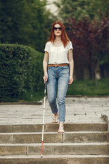 Wall Mural - Blind woman is walking on the sidewalk in city. Woman using a white cane.