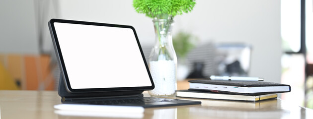 A white blank screen computer tablet with a keyboard case is putting on a table surrounded by various equipment.