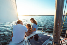 Family Of Three Sitting On Yacht Deck Sailing In Sea