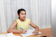 © SSTC STUDIO - Asian young little girl using pencil to do homework by herself. Student kid writing  homework book. Girl use computer to study at home. Education homeschool  concept.