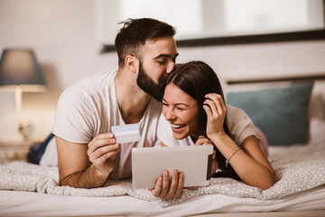 Wall Mural - Young couple shopping online from the comfort of bedroom and using digital tablet and credit card