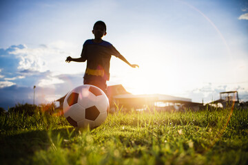 Boy kicking a ball while playing street soccer football on the green grass field for exercise. Outdoor sport activity for children and kids concept photo with copy space.