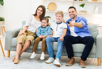  Family Of Four Watching TV Sitting On Sofa Indoors