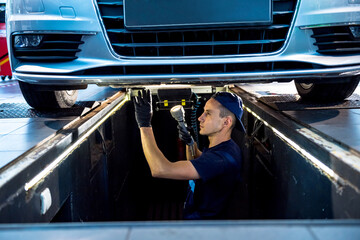 Wall Mural - Car mechanic examining car suspension of lifted automobile at service station