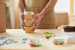 © Seventyfour - Close up of unrecognizable man wearing apron packaging orders while standing by wooden tables, food delivery service worker , copy space