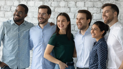 Wall Mural - Smiling motivated successful diverse employees team standing in modern office close up, looking to aside, posing for corporate photo, hugging, confident happy business people staff department