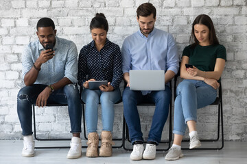 Wall Mural - Diverse candidates applicants seekers waiting for job interview, using mobile devices, laptop, smartphones, sitting on chairs in office hall, recruitment and human resources concept