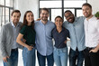 Smiling diverse business people, successful team, staff members hugging, standing in modern office, looking at camera, happy overjoyed employees colleagues posing for corporate photo
