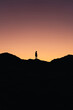 Vertical photo of a person standing in the middle of the mountain with the colors of the sunset in the background