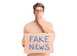 © Krakenimages.com - Young handsome man holding fake news banner covering mouth with hand, shocked and afraid for mistake. surprised expression