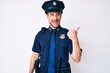 © Krakenimages.com - Young caucasian man wearing police uniform smiling with happy face looking and pointing to the side with thumb up.