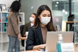 © Kawee - Asian young businesswoman wearing mask working on computer in office.