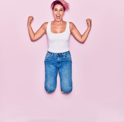 Young beautiful woman with pink short hair wearing casual clothes smiling happy. Jumping with smile on face celebrating with fists up over isolated background.