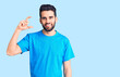 © Krakenimages.com - Young handsome man with beard wearing casual t-shirt smiling and confident gesturing with hand doing small size sign with fingers looking and the camera. measure concept.
