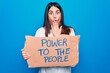 © Krakenimages.com - Young woman asking for social movement holding banner with power to the people message covering mouth with hand, shocked and afraid for mistake. Surprised expression