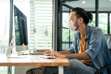 Asian young businessman wearing mask working on computer in office.