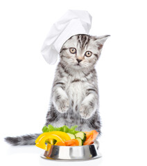 Poster - Cute kitten wearing chef's hat stands with bowl of the vegetables. Isolated on white background