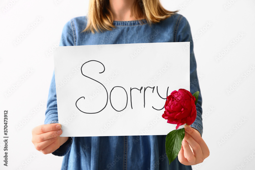 Woman holding paper with word SORRY on white background, closeup - obrazy, fototapety, plakaty 