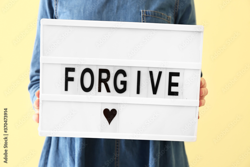 Woman holding board with word FORGIVE on color background, closeup - obrazy, fototapety, plakaty 