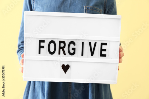 Cuadros en Lienzo Woman holding board with word FORGIVE on color background, closeup