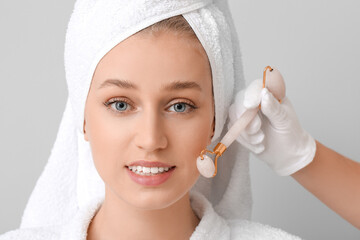 Canvas Print - Young woman receiving facial massage on grey background