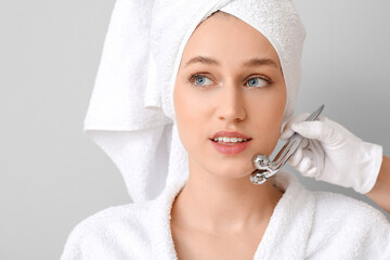 Canvas Print - Young woman receiving facial massage on grey background