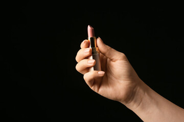 Hand with beautiful manicure holding lipstick on dark background