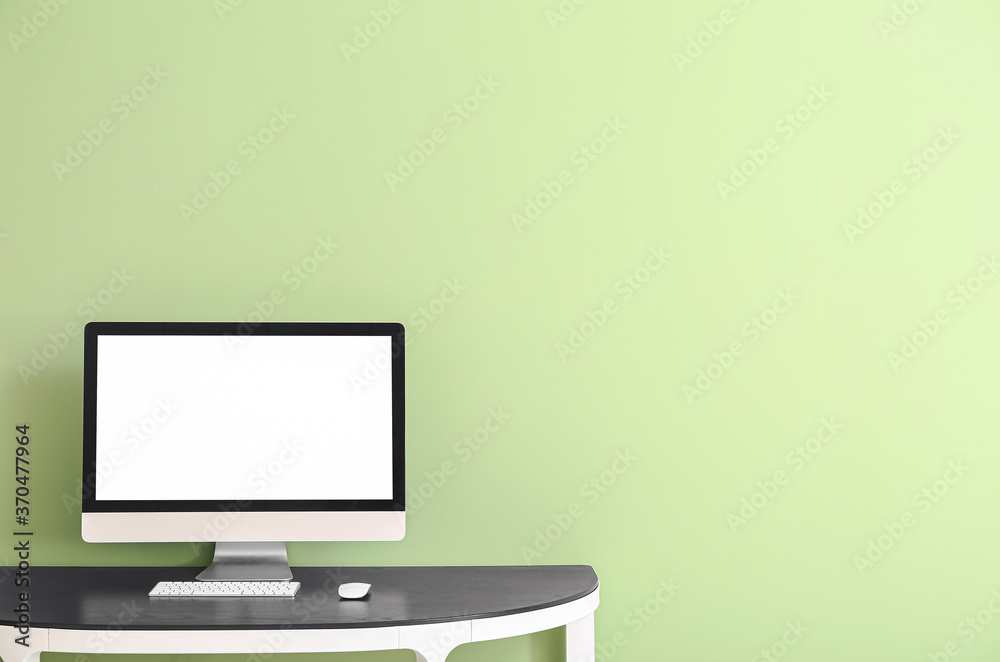 Modern computer on table near color wall
