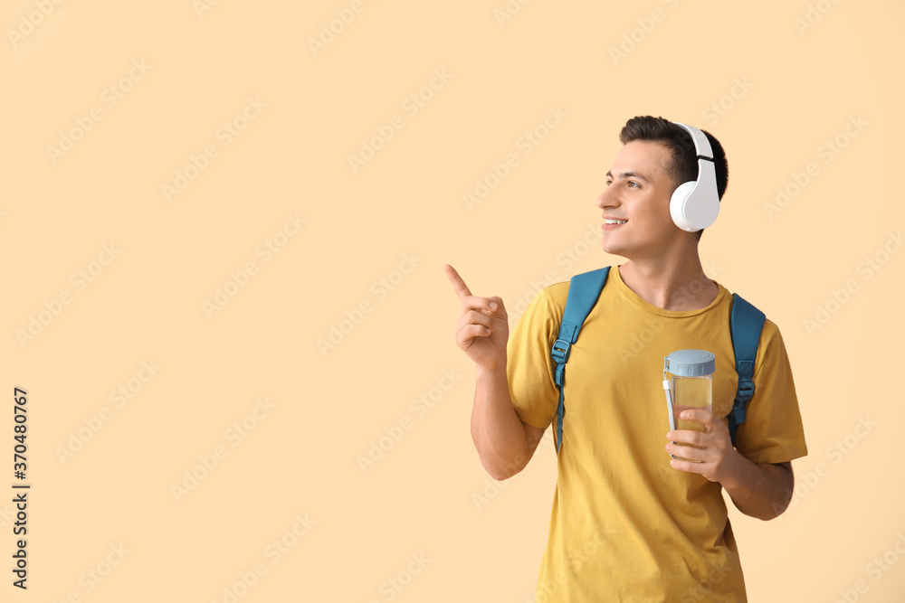 Young man with bottle of water and headphones pointing at something on color background - obrazy, fototapety, plakaty 