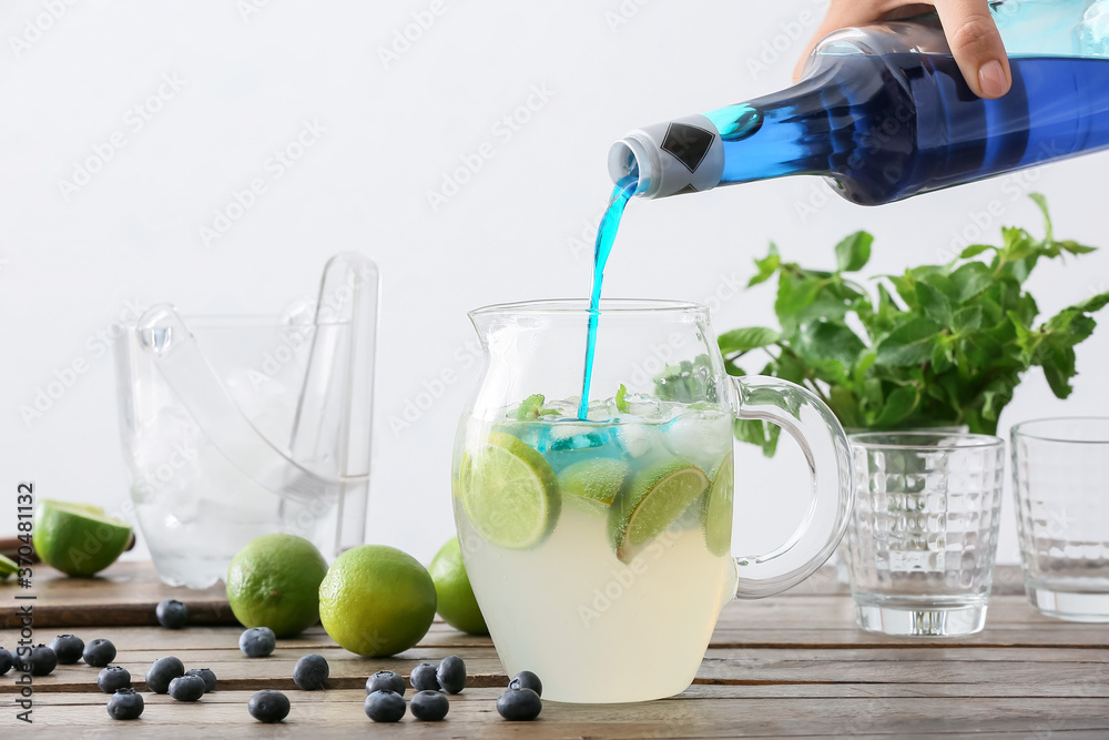 Woman making tasty blue mojito cocktail at table