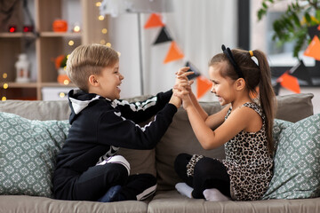 Poster - halloween, holiday and childhood concept - smiling little boy and girl in costumes having fun at home