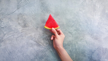 Wall Mural - Woman's hand holding a piece of fresh watermelon isolated on grey or gray wall background with copy space. Rough or loft style wallpaper and Freshness fruit on summertime concept 